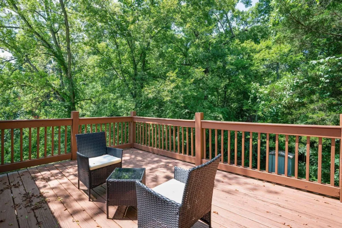 A peaceful exterior deck space with comfortable outdoor seating is surrounded by mature trees. The area invites relaxation, reading, or social time with family, embraced by natural light and greenery.