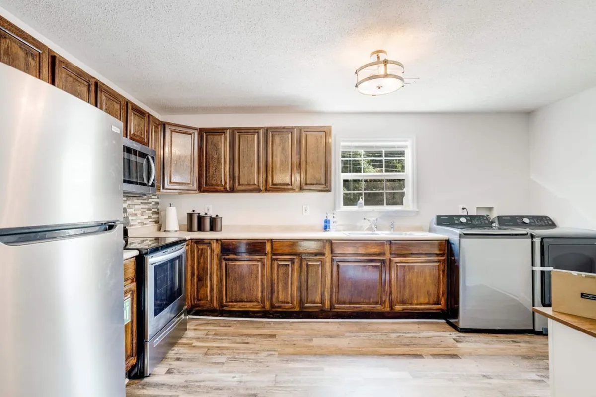 A bright, modern kitchen equipped with stainless steel appliances, cabinetry, a window streaming with natural light, and visible laundry appliances. The space feels comfortable and functional, ideal for meal prep or family gatherings.