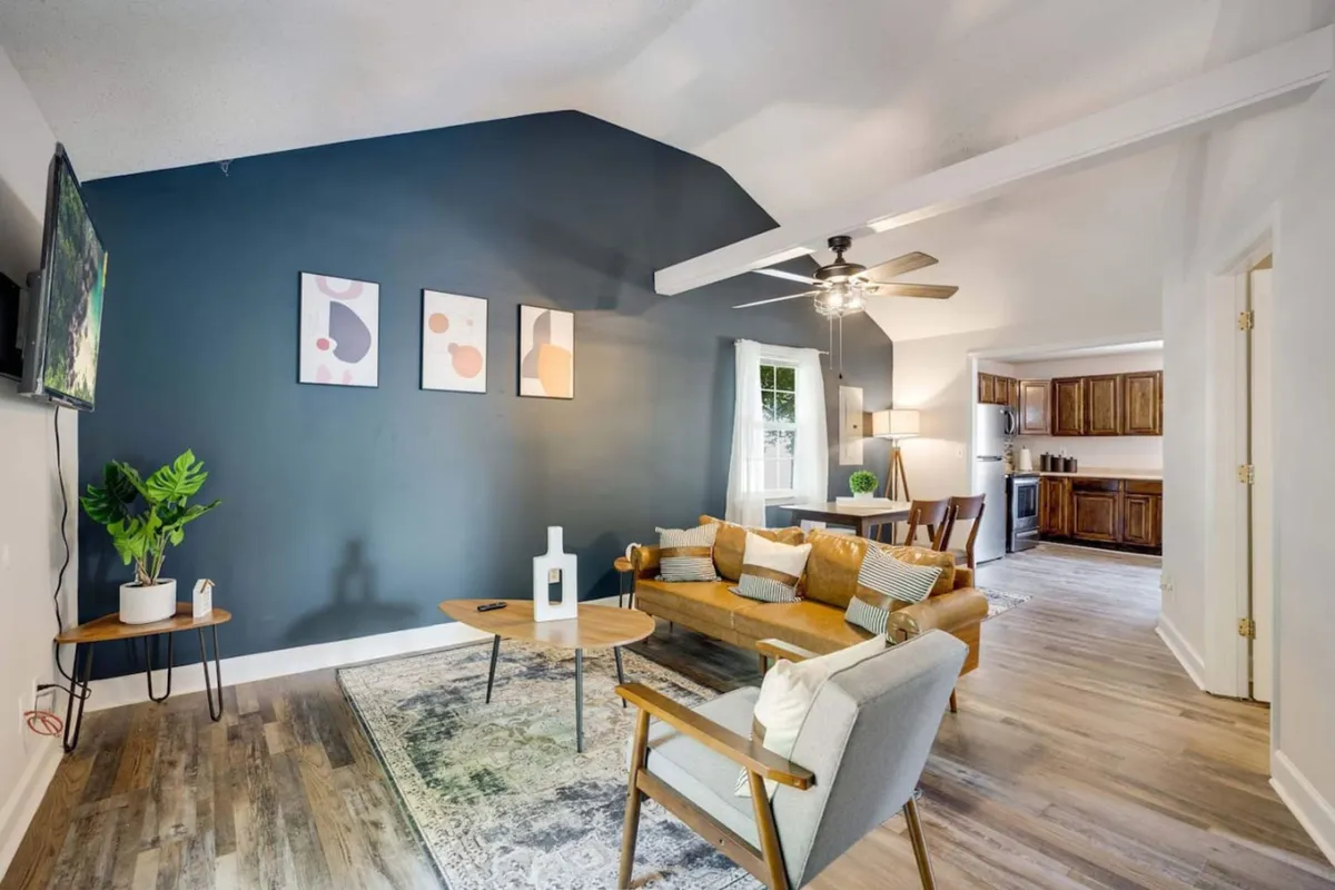 The image showcases a warm, inviting living room with a plush sofa, a stylish coffee table, vibrant artwork adorning the wall, a flat-screen television, and a touch of greenery from a house plant. The space is bathed in soft, natural light and designed for comfort and relaxation, perfect for socializing or unwinding after a day exploring downtown Clarksville.