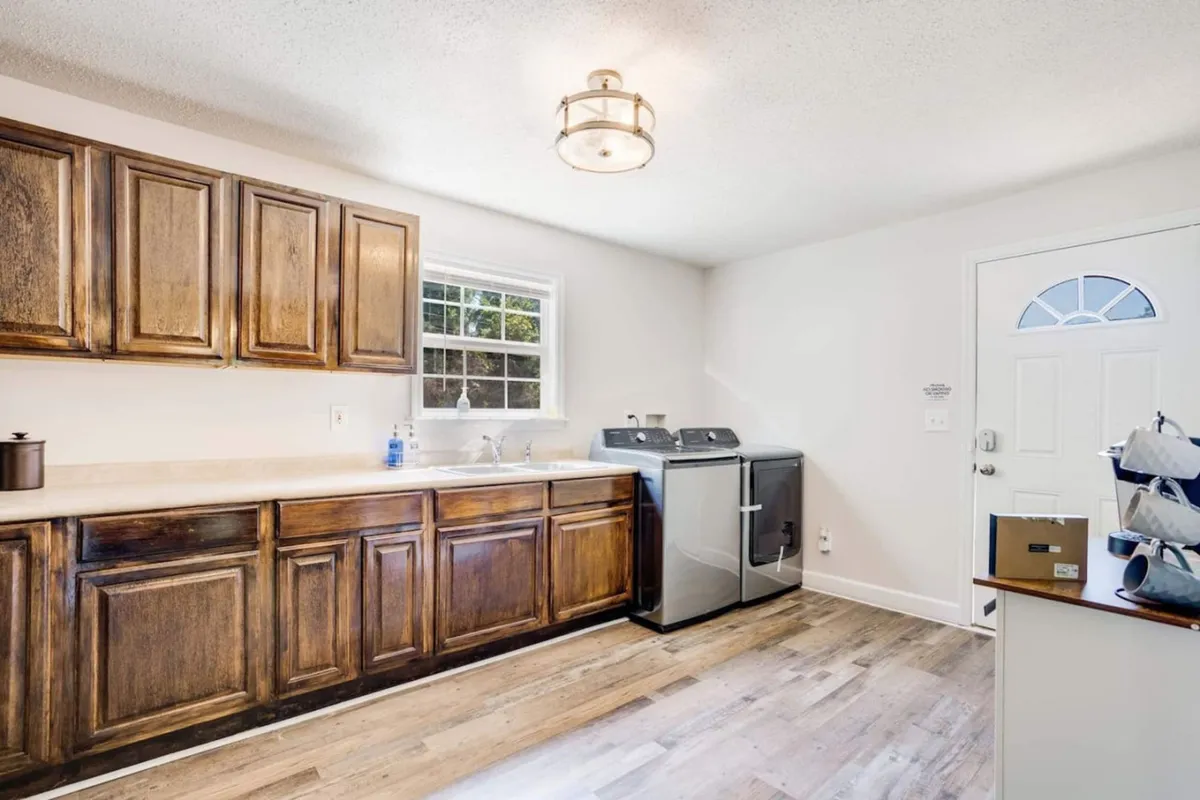 A functional laundry area with wooden cabinets, a front-loading washing machine, and a sink, all set near the home’s entryway. The space is tidy and practical, blending utility with welcoming design.